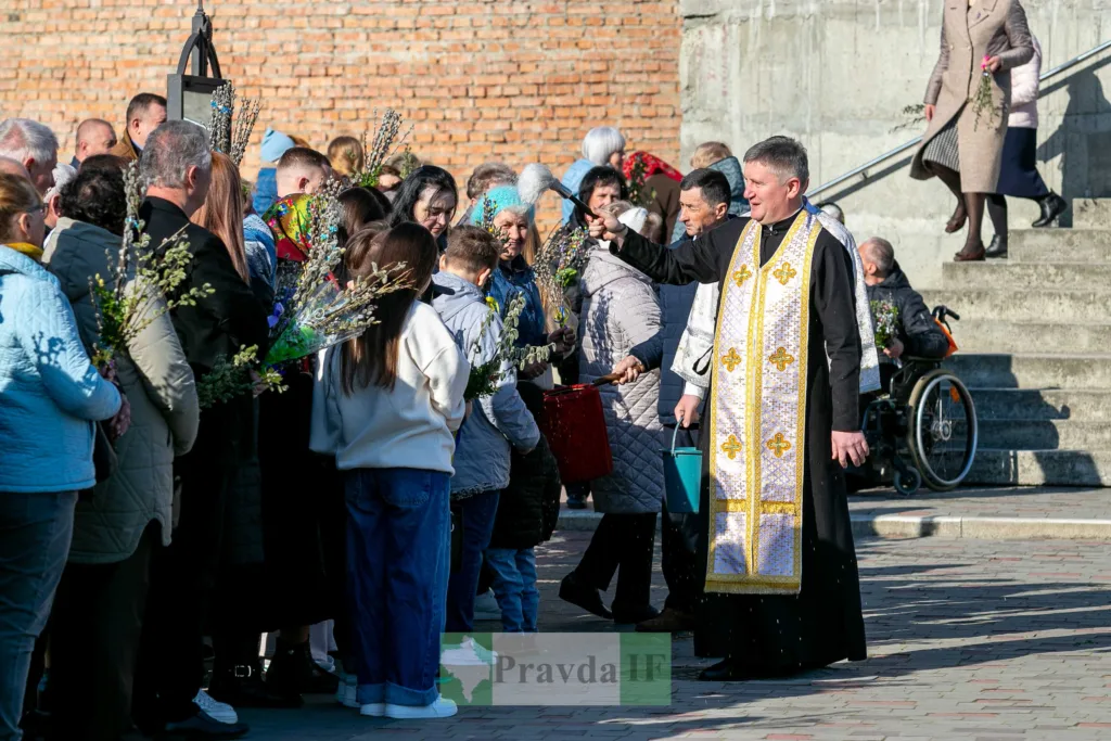Священник окроплює вірян свяченою водою на вулиці
