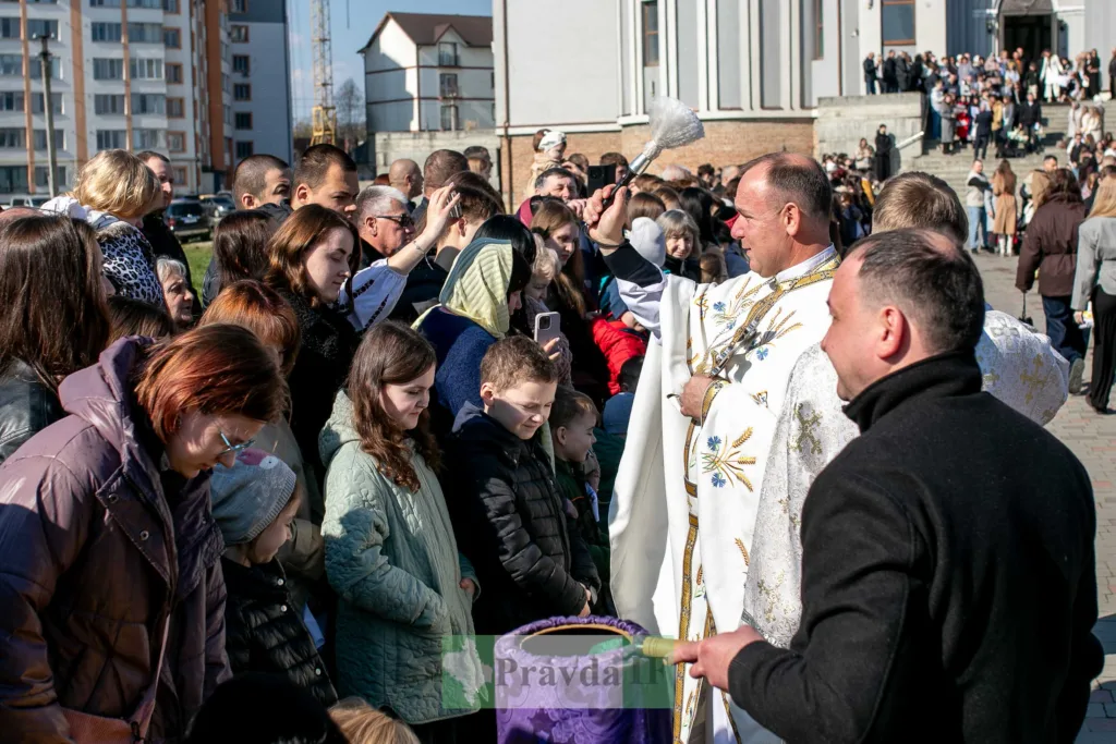Священник окроплює прихожан святою водою біля церкви