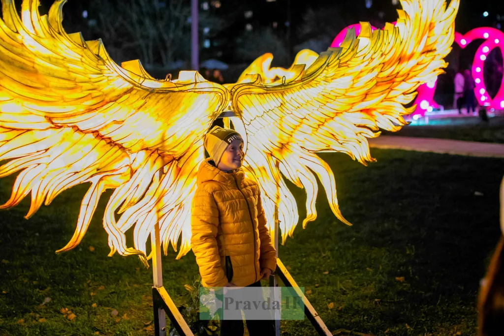 Дитина біля світлових крил на нічному фестивалі
