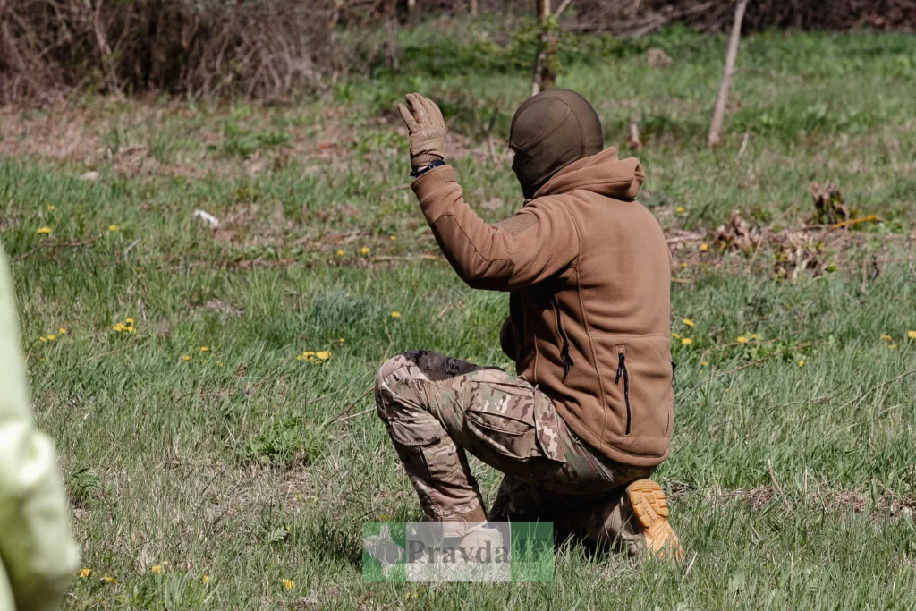 Військовий у камуфляжі на траві піднімає руку