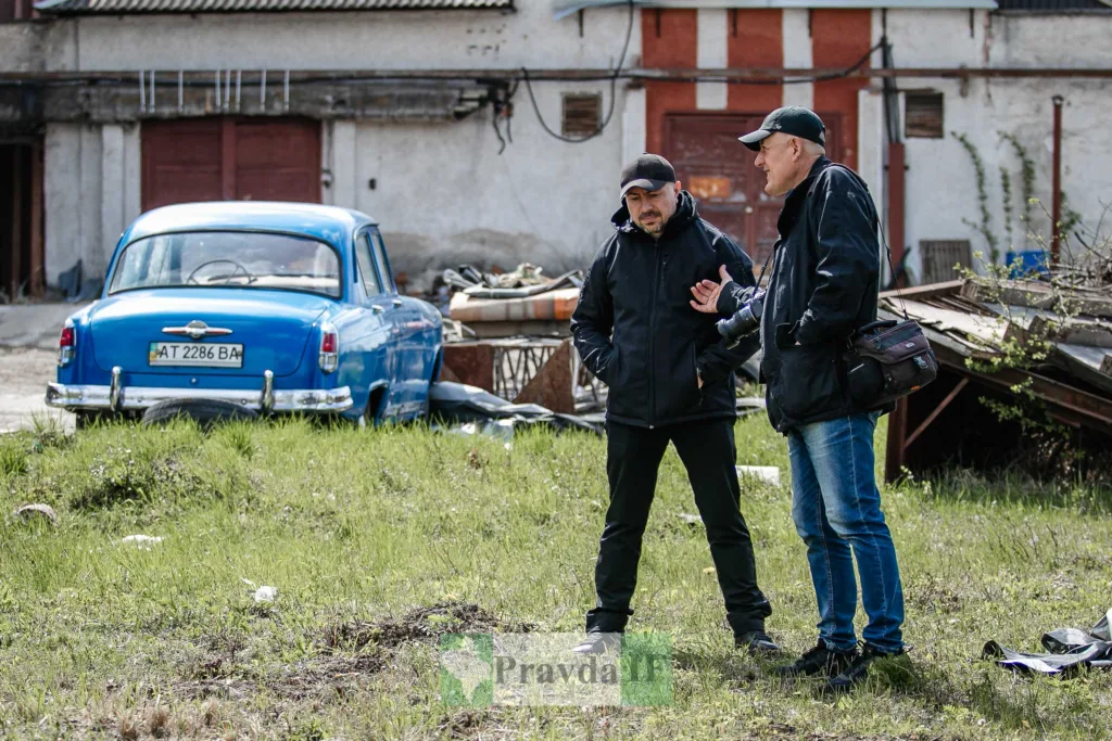 Двоє чоловіків розмовляють біля старого синього авто