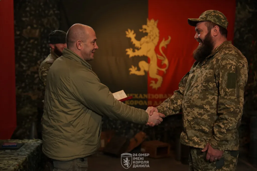 Військові потискають руки перед прапором бригади