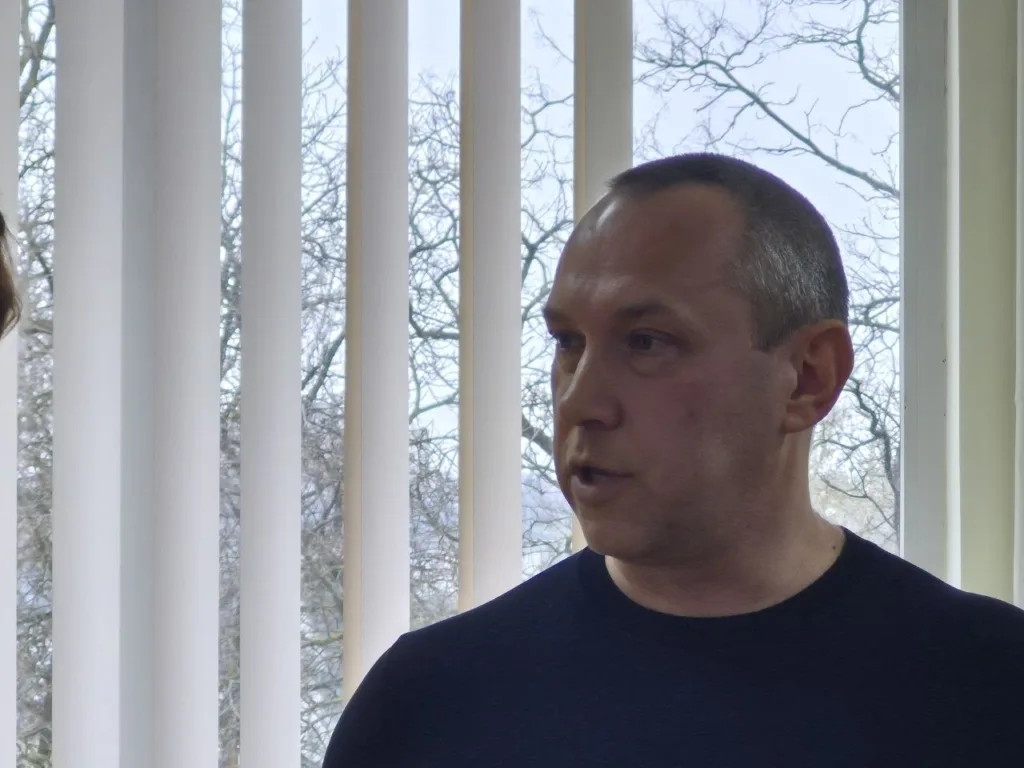 Чоловік розмовляє біля вікна з жалюзі