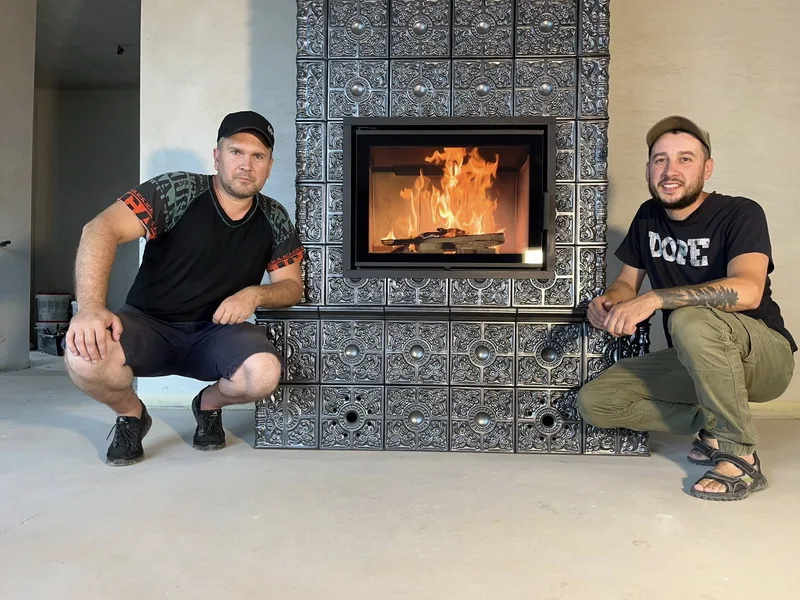Двоє чоловіків біля кахельного каміна з вогнем