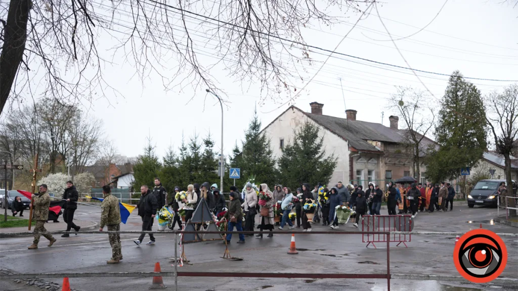 Люди йдуть вулицею з квітами та прапорами