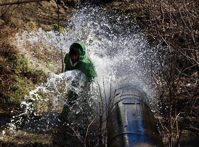 Витік води з труби, робітник у дощовику