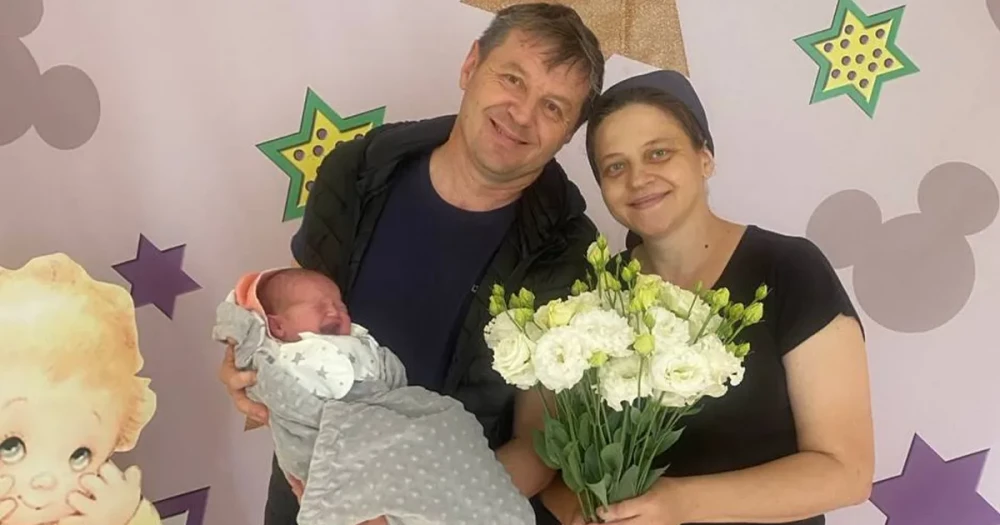 Подружжя тримає немовля і букет квітів