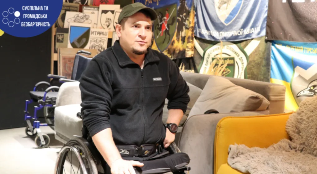 Чоловік у візку перед стінами з прапорами