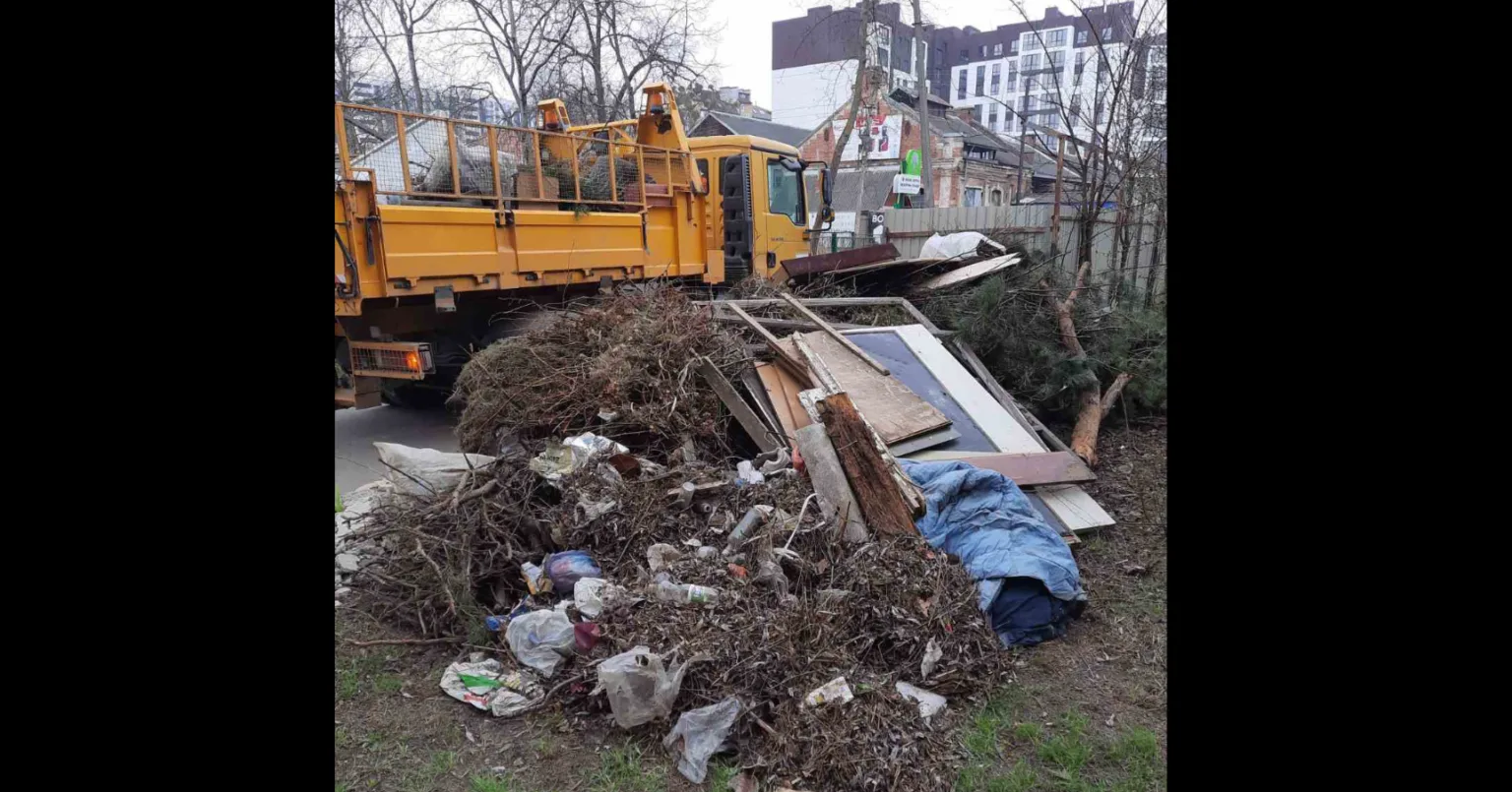 Жовта вантажівка збирає купу сміття та гілок
