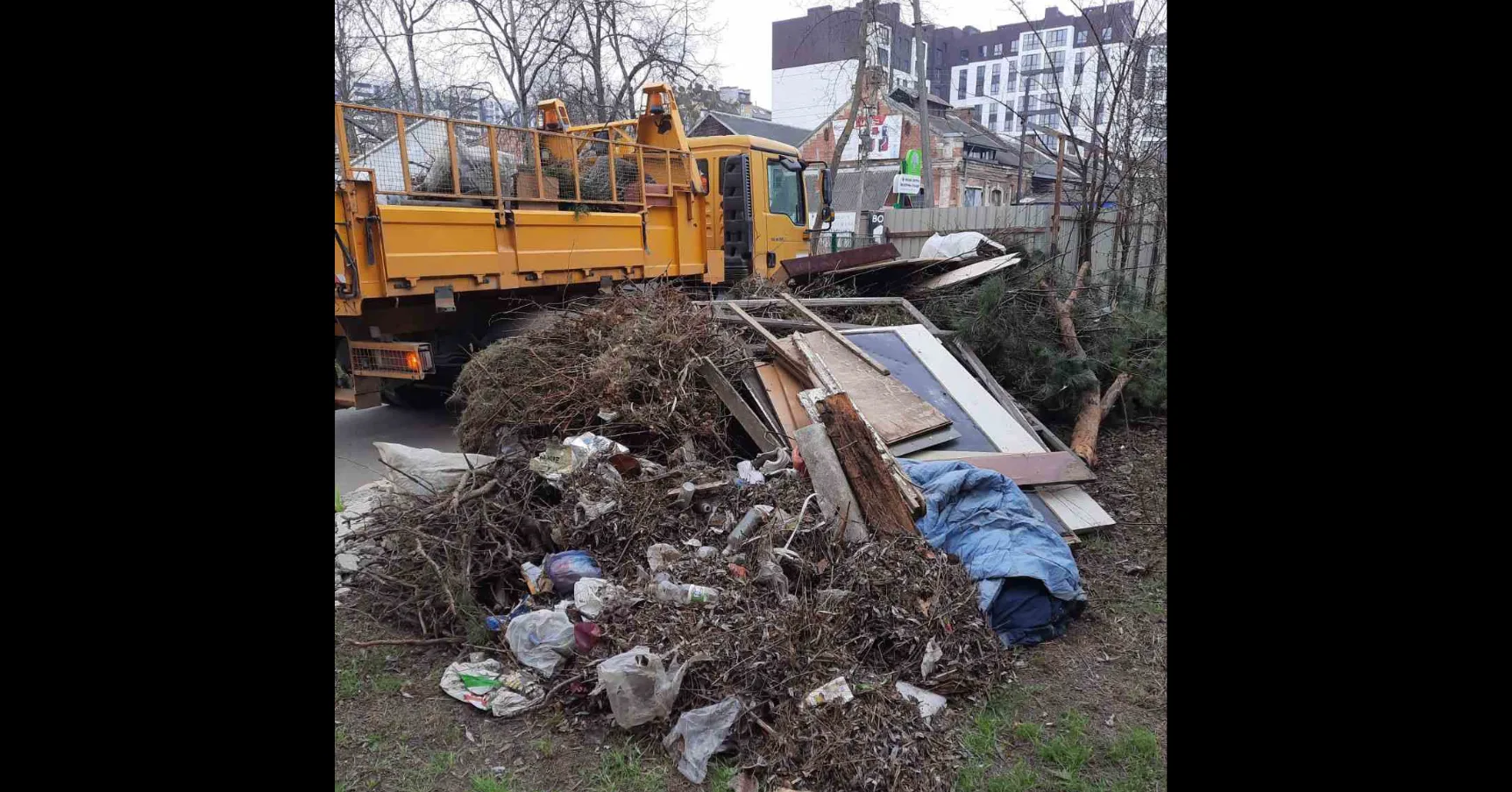 Жовта вантажівка збирає купу сміття та гілок