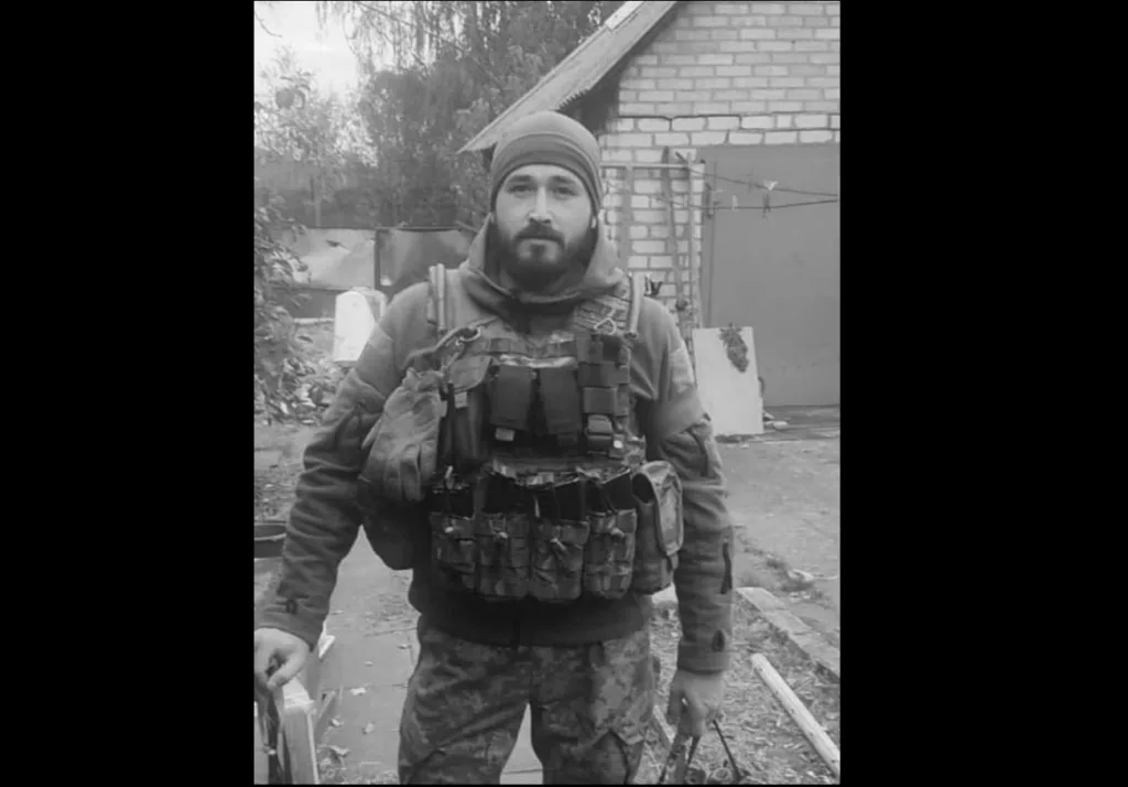 Військовий у спорядженні стоїть біля будинку