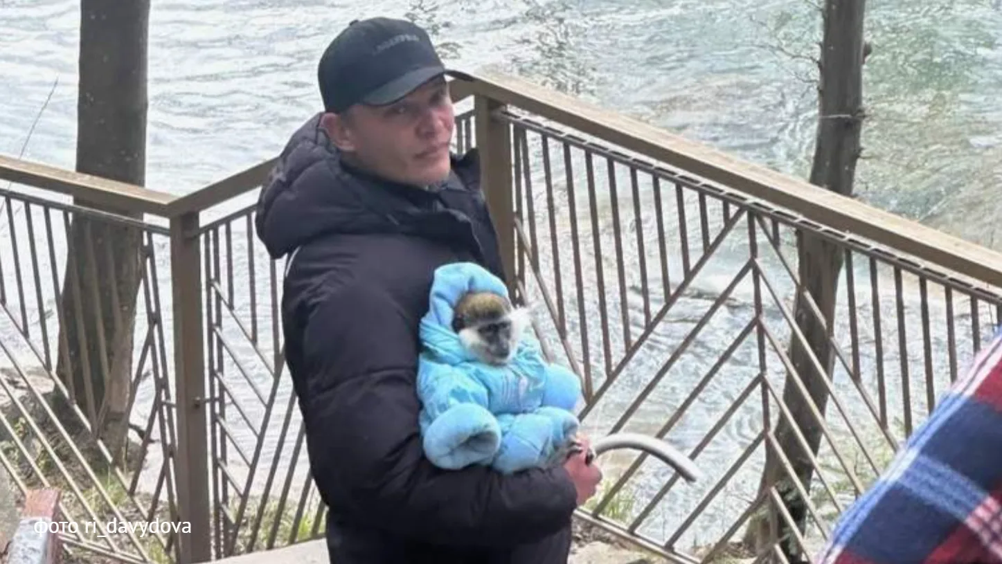 Чоловік тримає мавпу в синьому комбінезоні