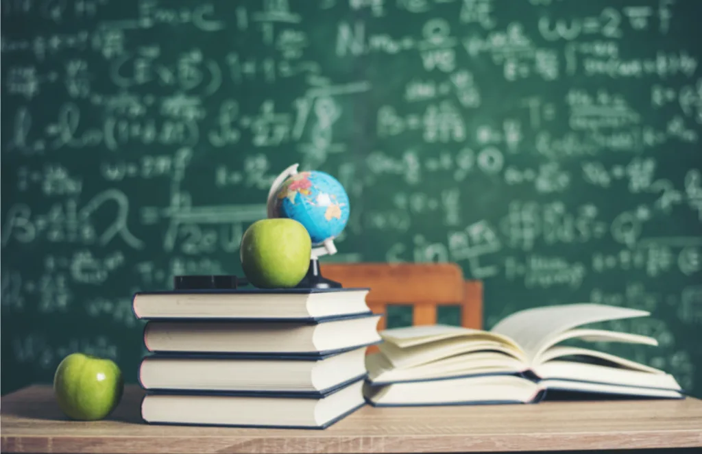 Книги, яблука і глобус перед шкільною дошкою