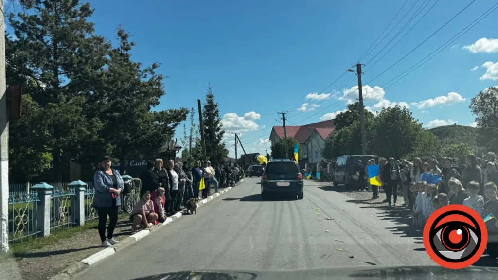 Люди з українськими прапорами стоять вздовж дороги