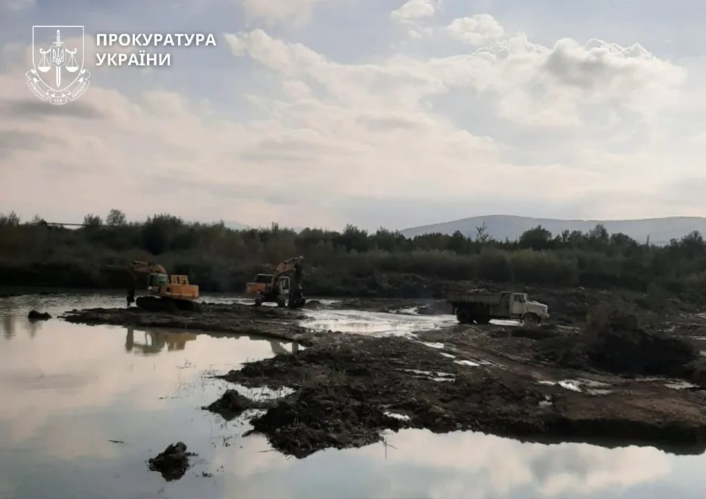 Екскаватори працюють біля річки серед гірського пейзажу
