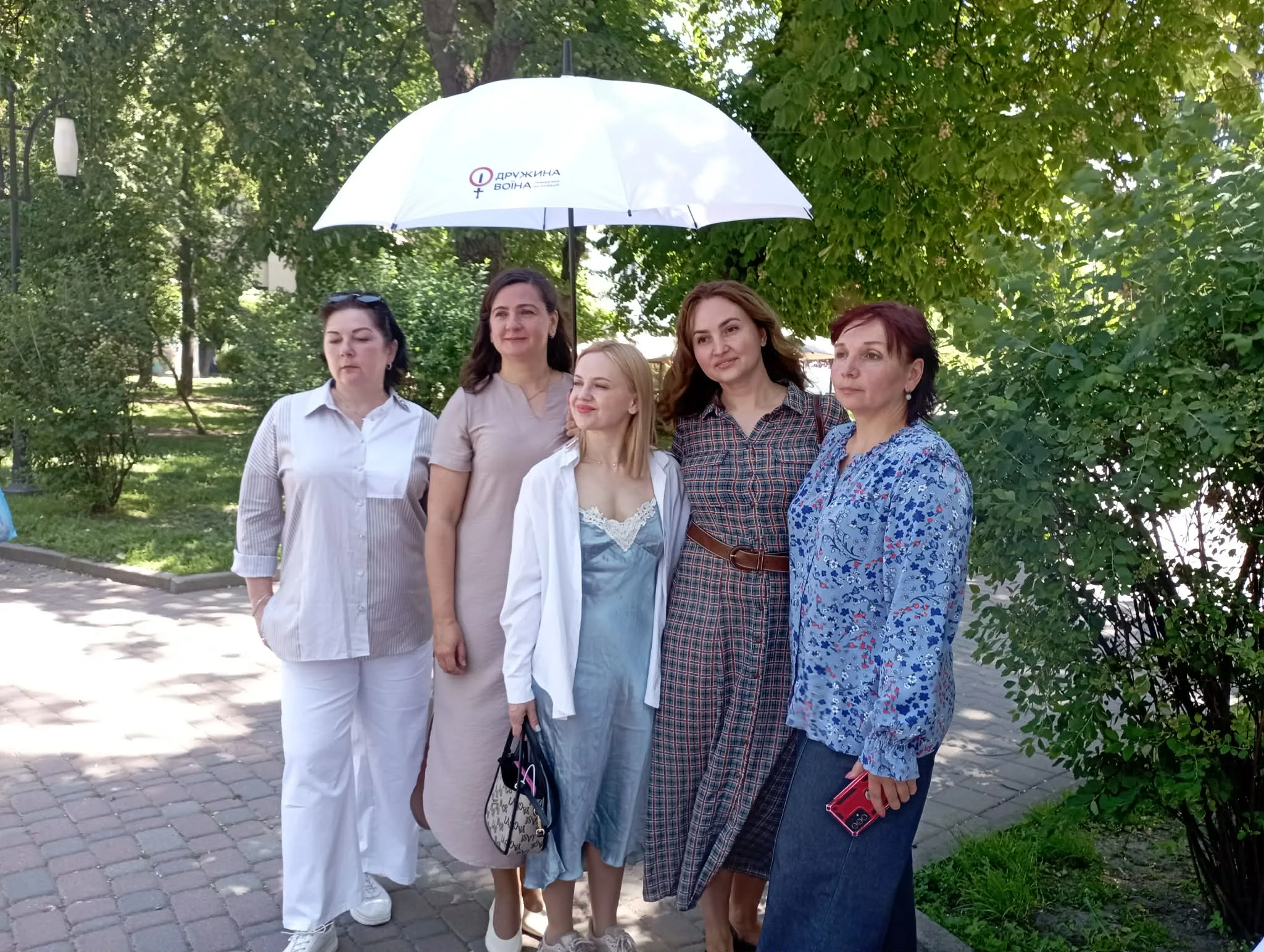 П'ять жінок стоять під парасолькою у парку