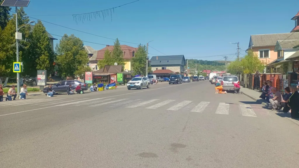 Люди на колінах біля дороги з автоколоною