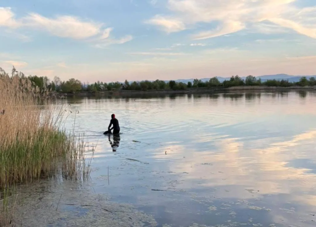 Людина у воді біля озера на заході сонця