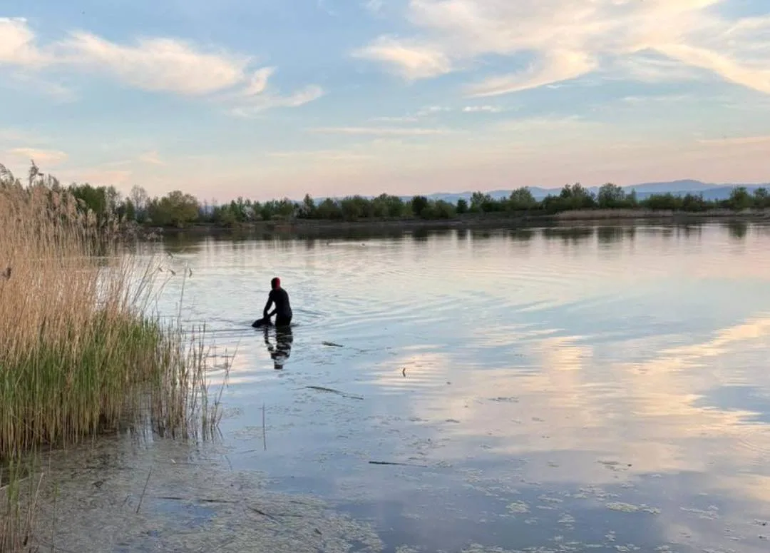 Людина у воді біля озера на заході сонця