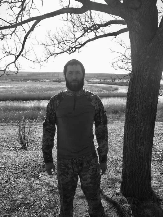 Чоловік у камуфляжі стоїть біля дерева на природі