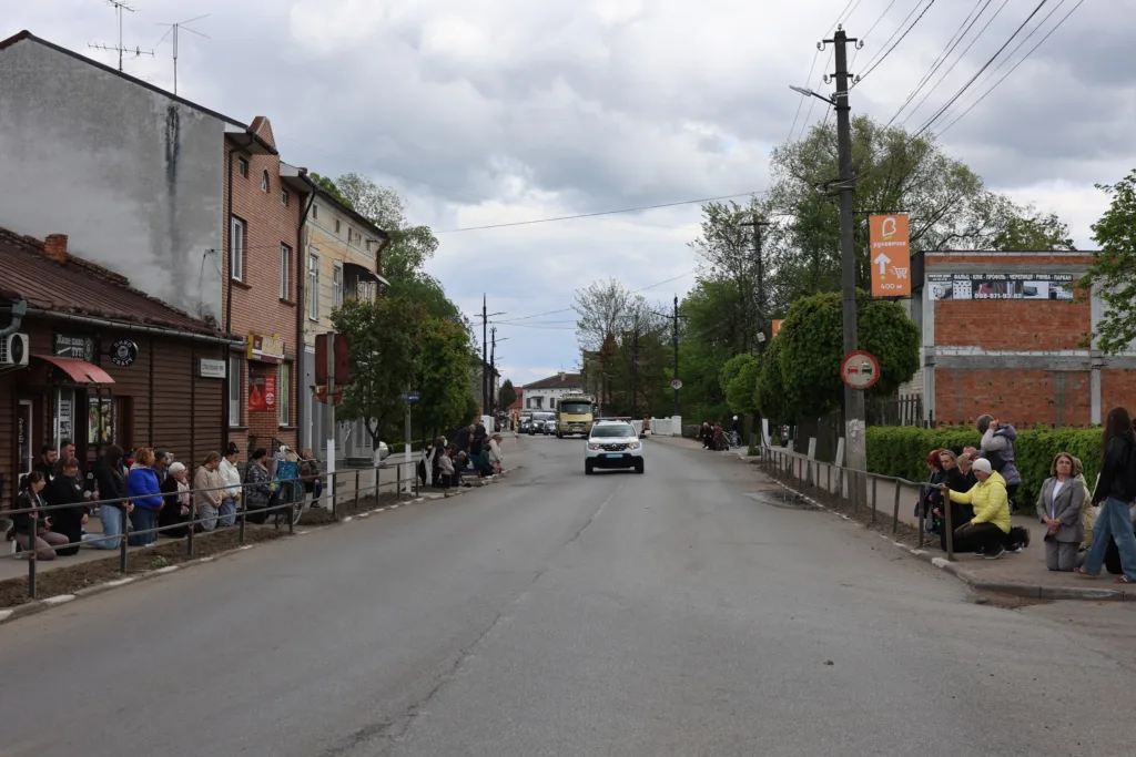Люди стоять уздовж дороги в невеликому місті