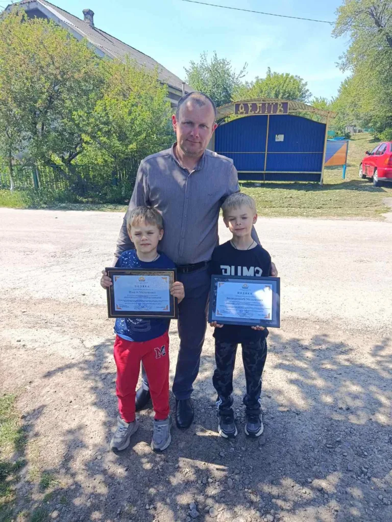 Чоловік і двоє дітей тримають грамоти на вулиці