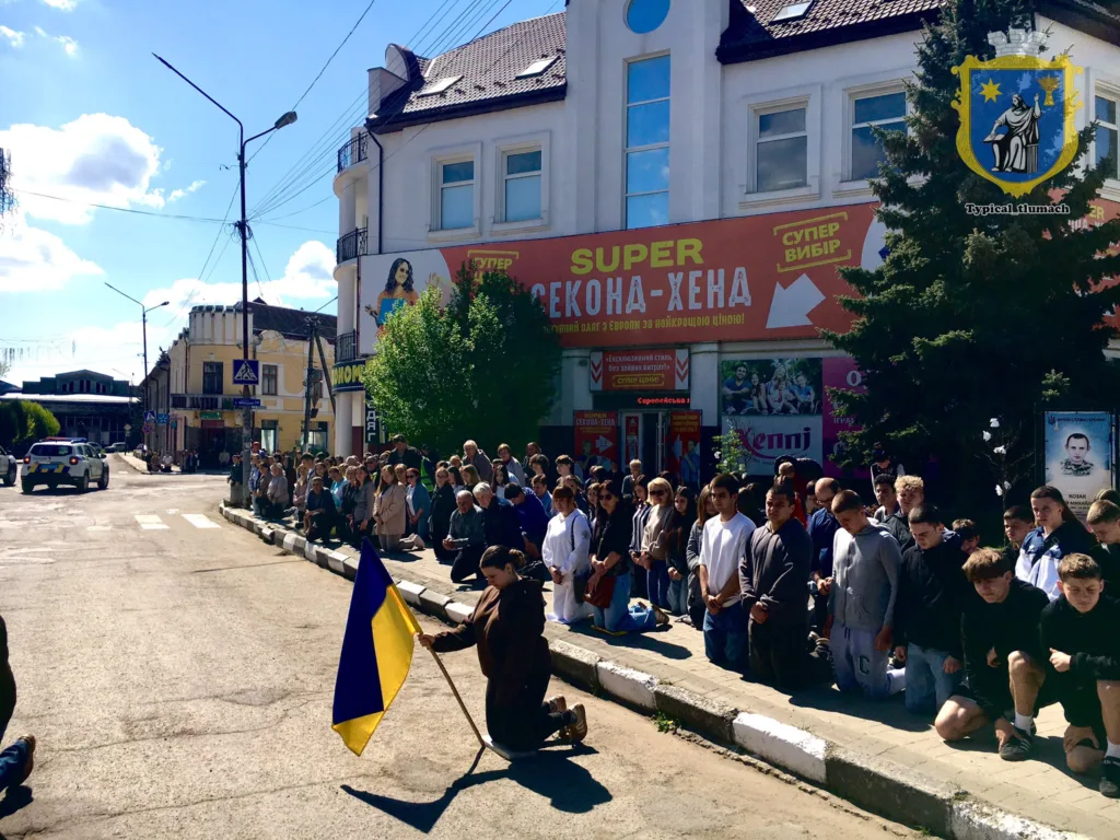 Люди стоять на колінах з українським прапором на вулиці