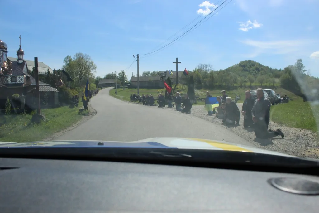 Люди на колінах уздовж дороги з прапорами України