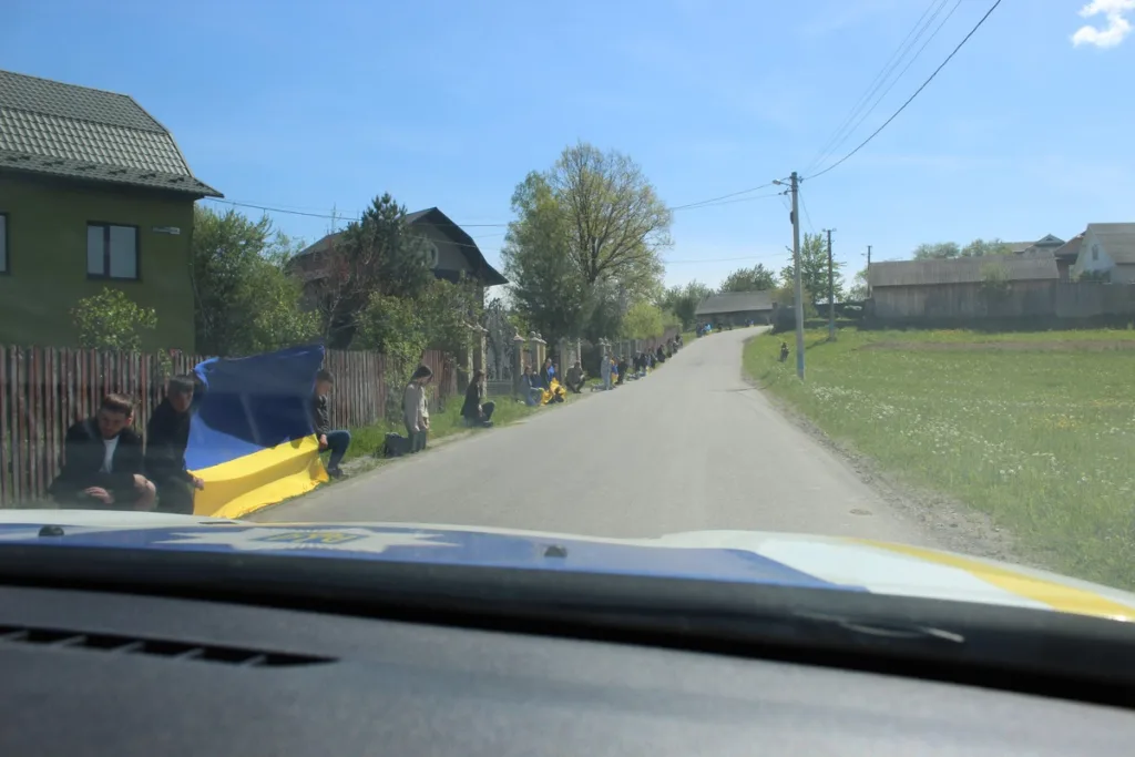 Люди з українським прапором стоять вздовж дороги