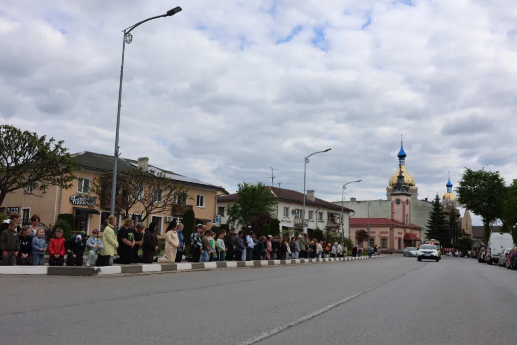 Люди стоять уздовж дороги біля церкви