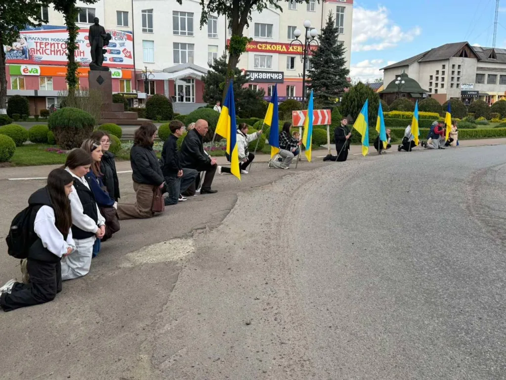 Люди на колінах з українськими прапорами на вулиці