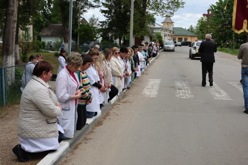 Люди стоять на колінах уздовж дороги під час процесії