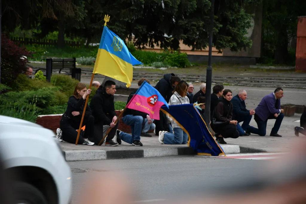 Люди на колінах з українськими прапорами