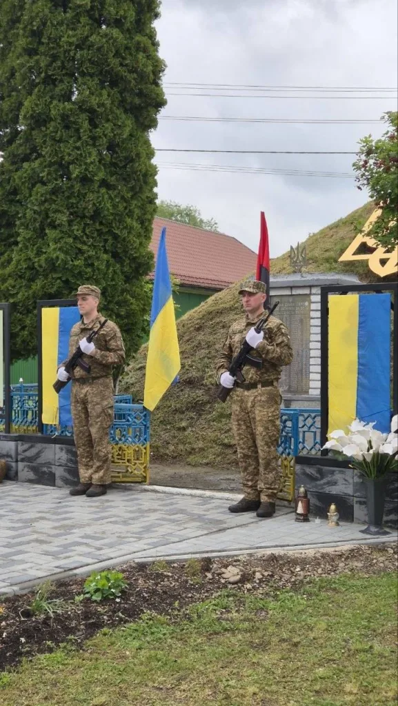 Українські військові стоять біля меморіалу з прапорами