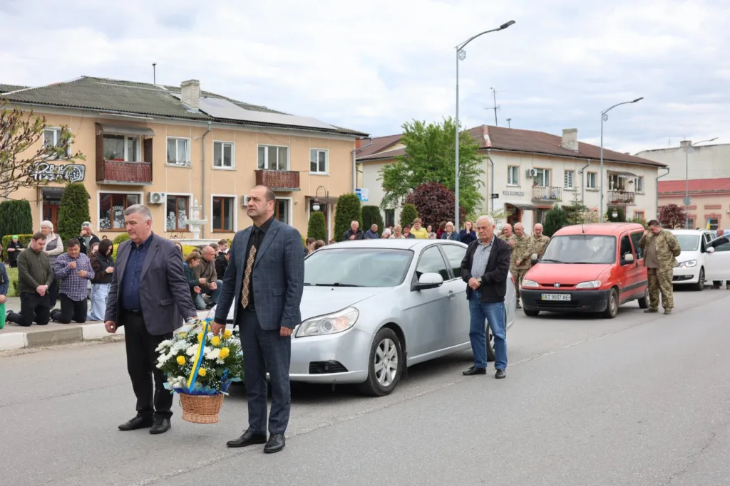 Люди стоять і кладуть квіти на міській вулиці