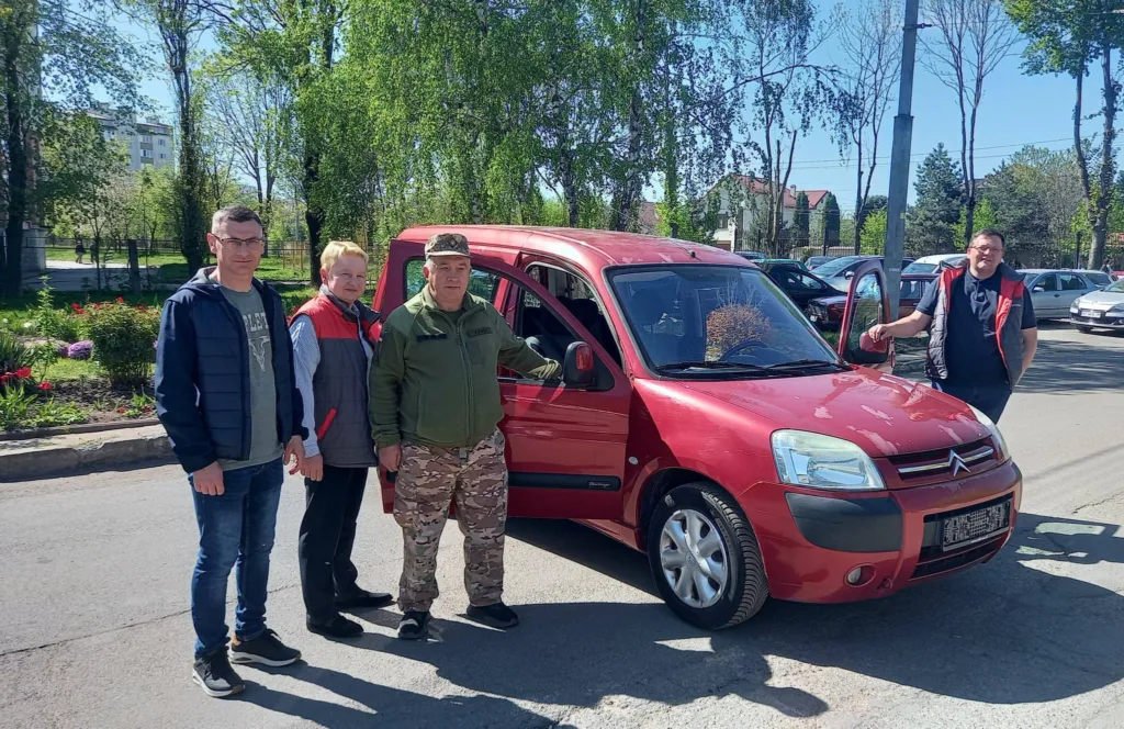 Люди стоять біля червоного автомобіля на вулиці