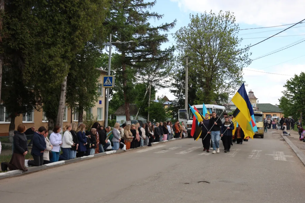 Люди з українськими прапорами йдуть вулицею міста