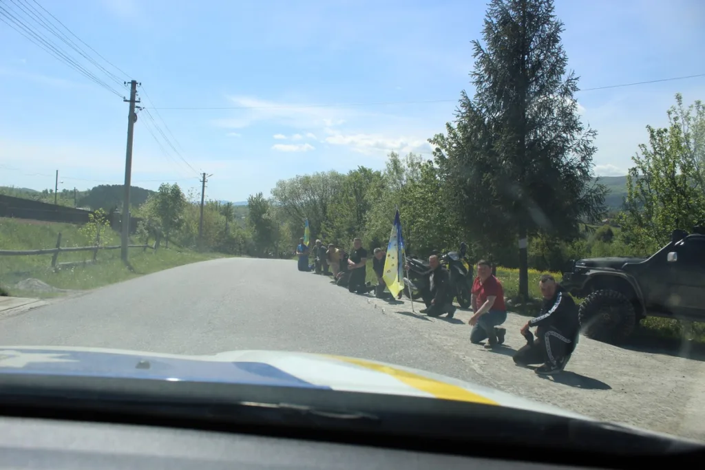 Люди на колінах уздовж дороги з прапорами України
