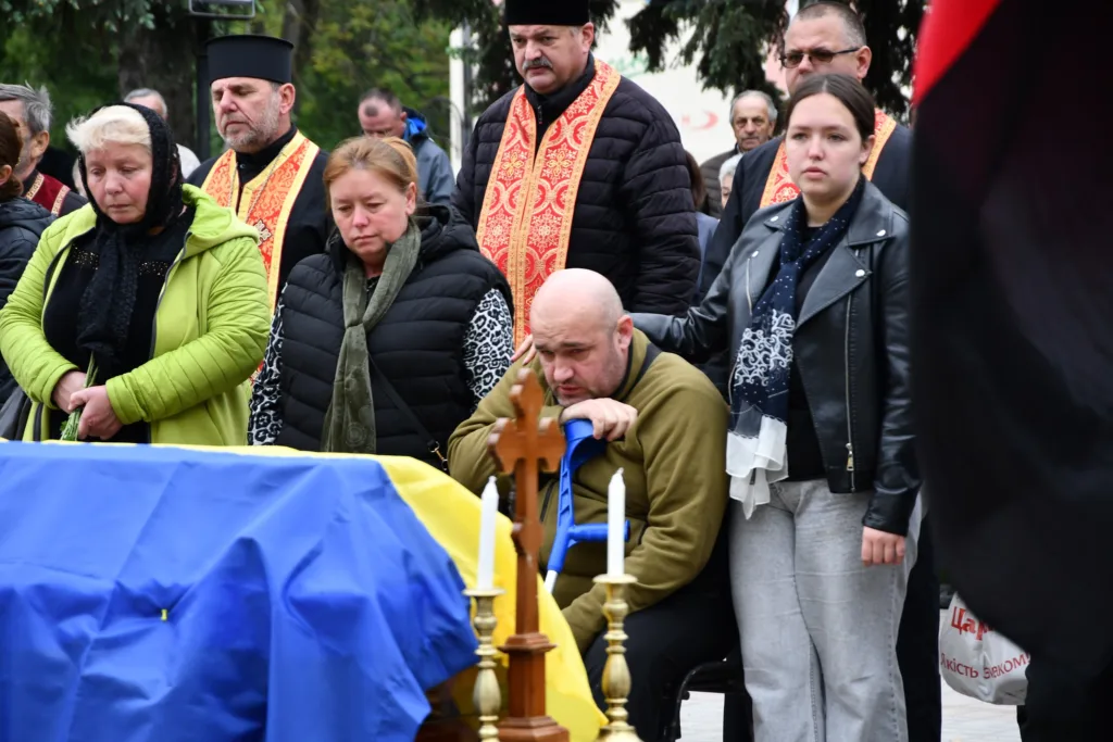 Люди оплакують полеглого героя біля труни з прапором
