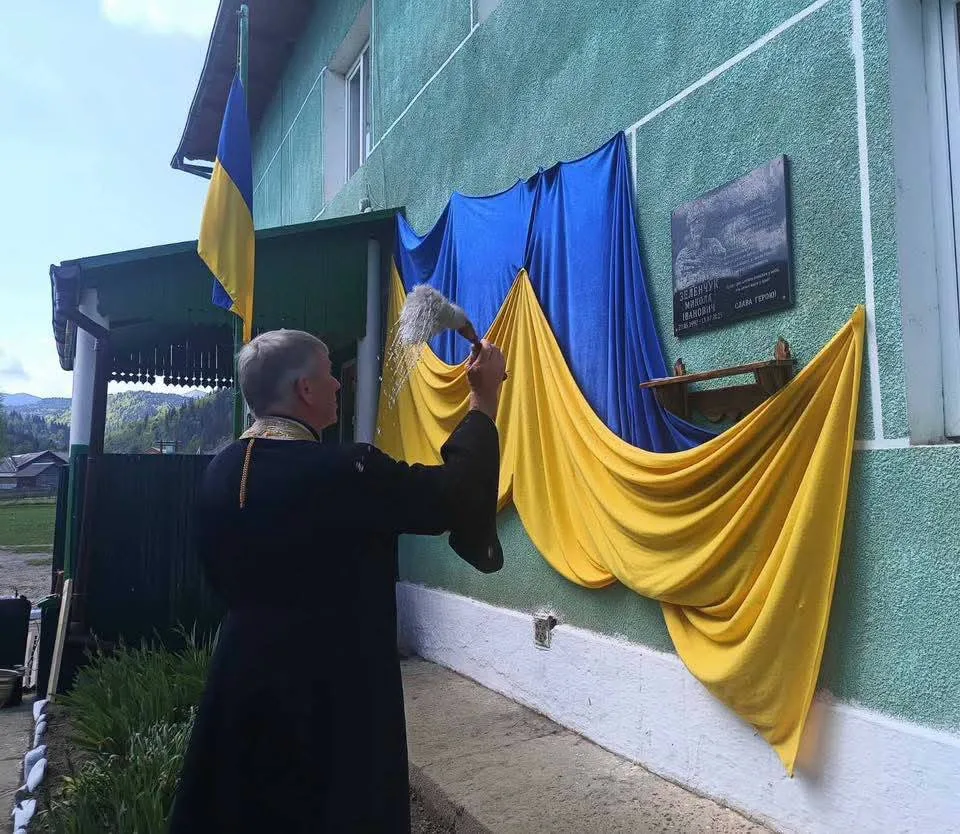 Священник освячує меморіальну дошку з прапором України