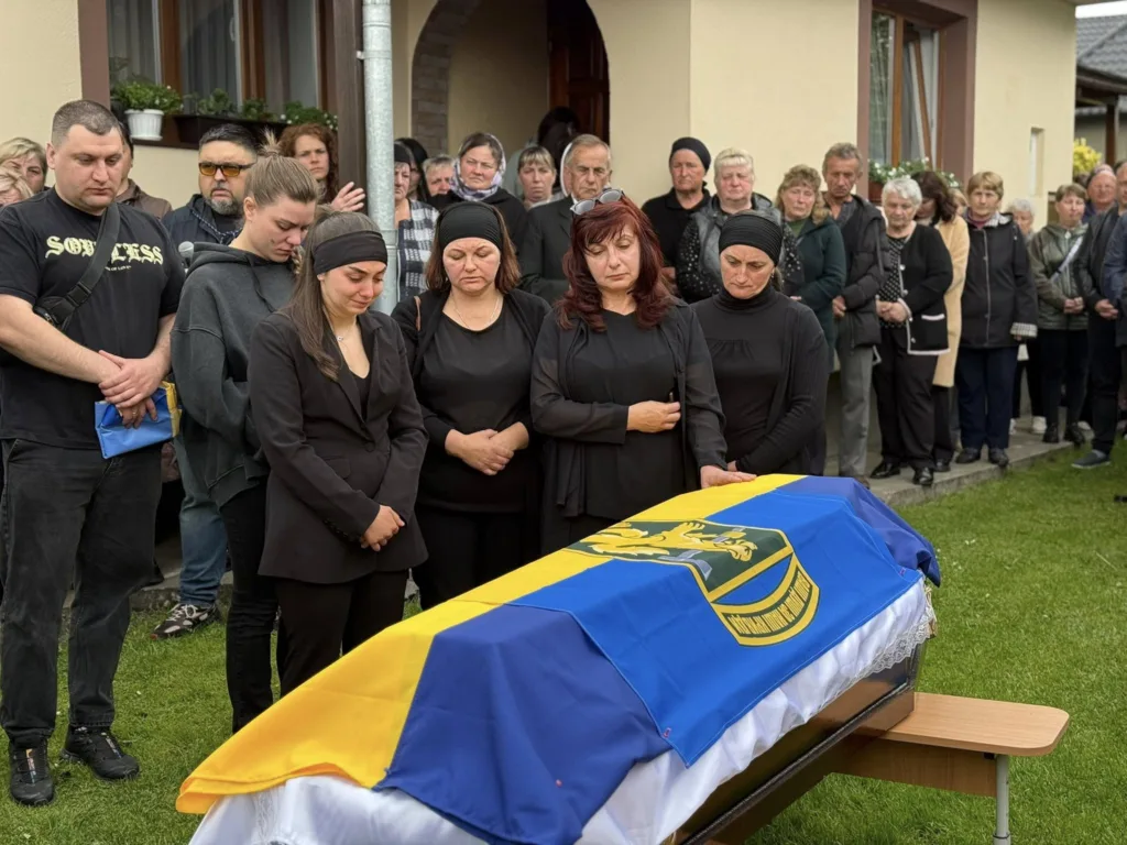Люди оплакують труну, накриту українським прапором