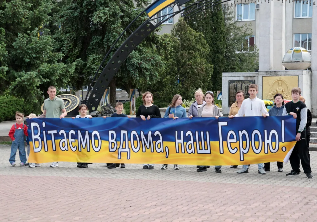 Люди тримають банер із написом Вітаємо вдома наш Герою