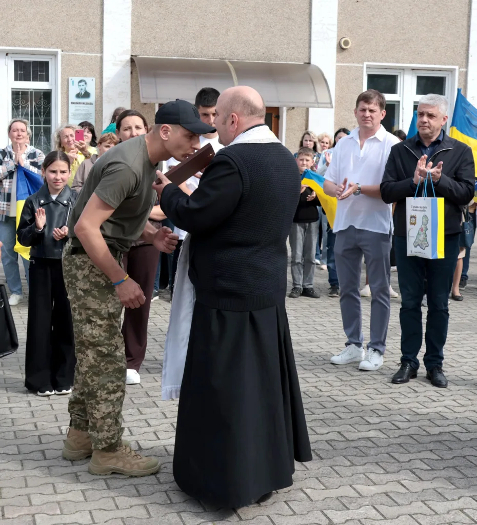 Священник благословляє українського військового серед людей