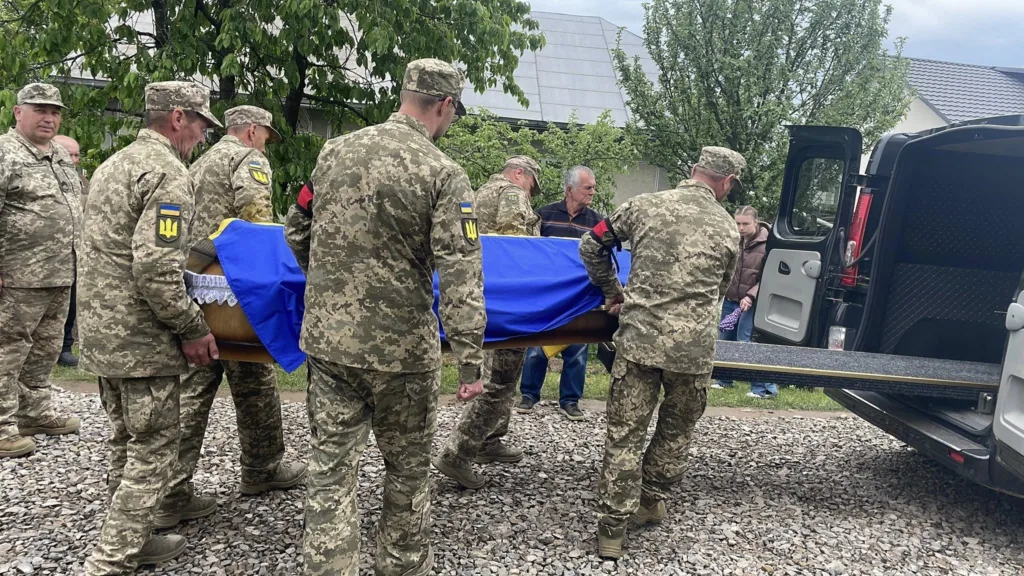 Військові несуть труну, накриту українським прапором