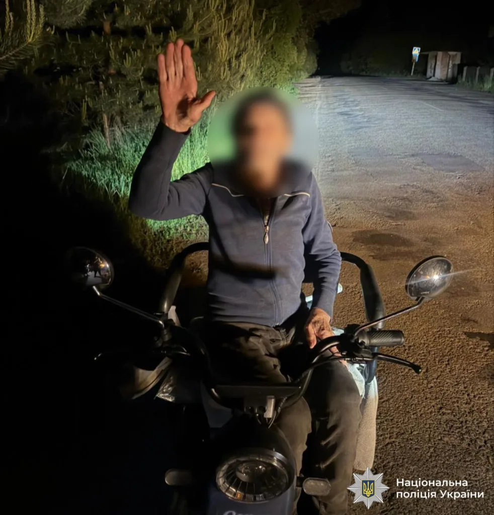 Чоловік на мопеді вночі піднімає руку