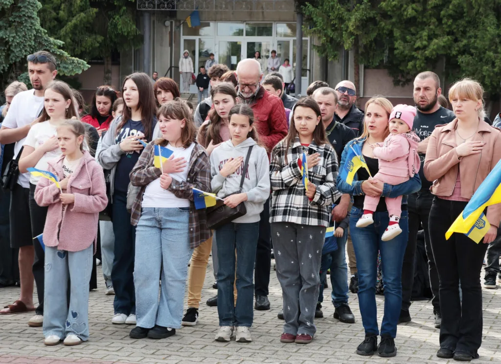 Люди співають гімн України, тримаючи прапори