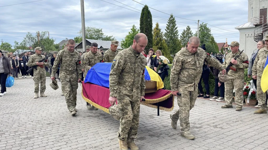 Військові несуть труну, накриту українським прапором