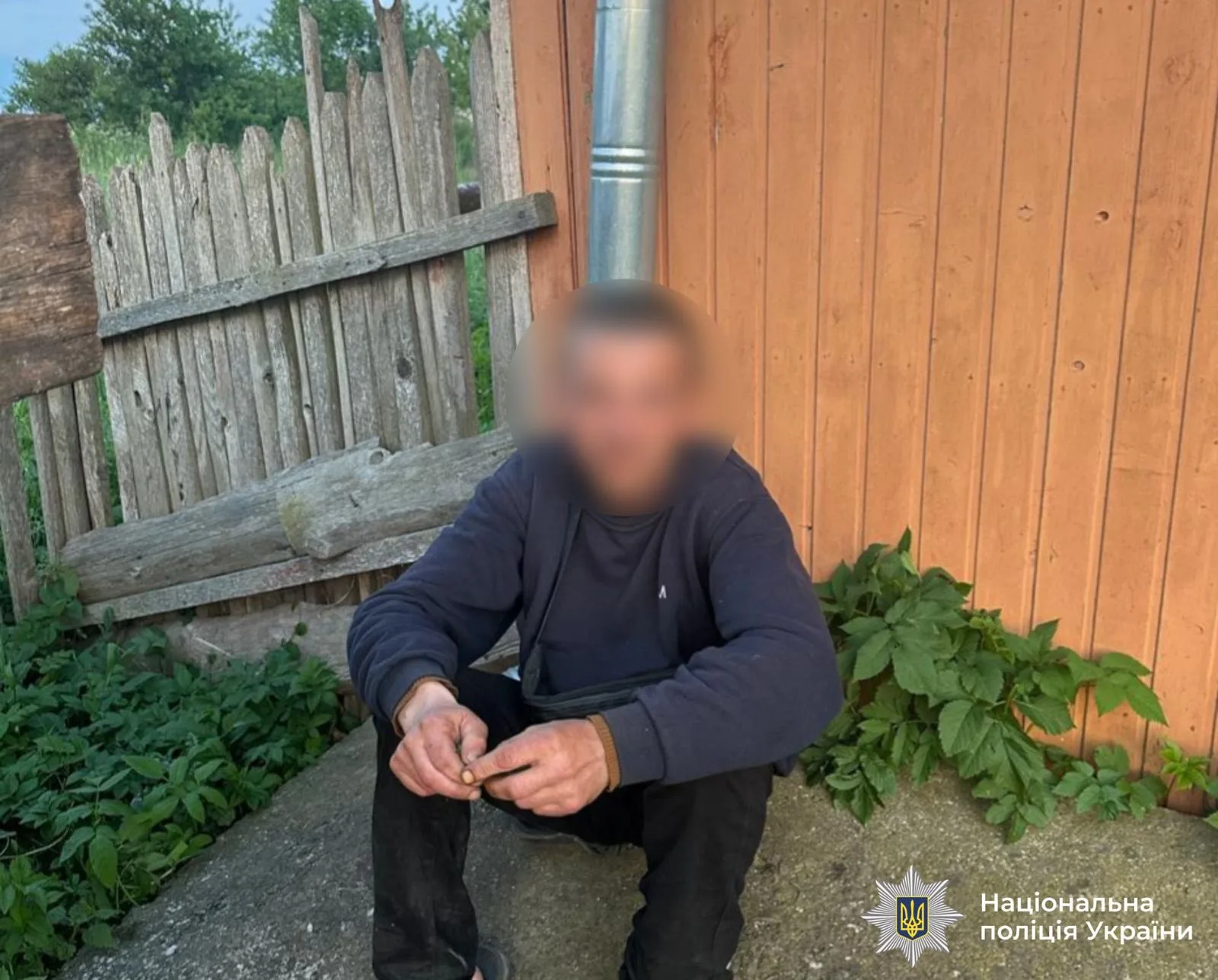 Чоловік сидить біля дерев'яного паркану