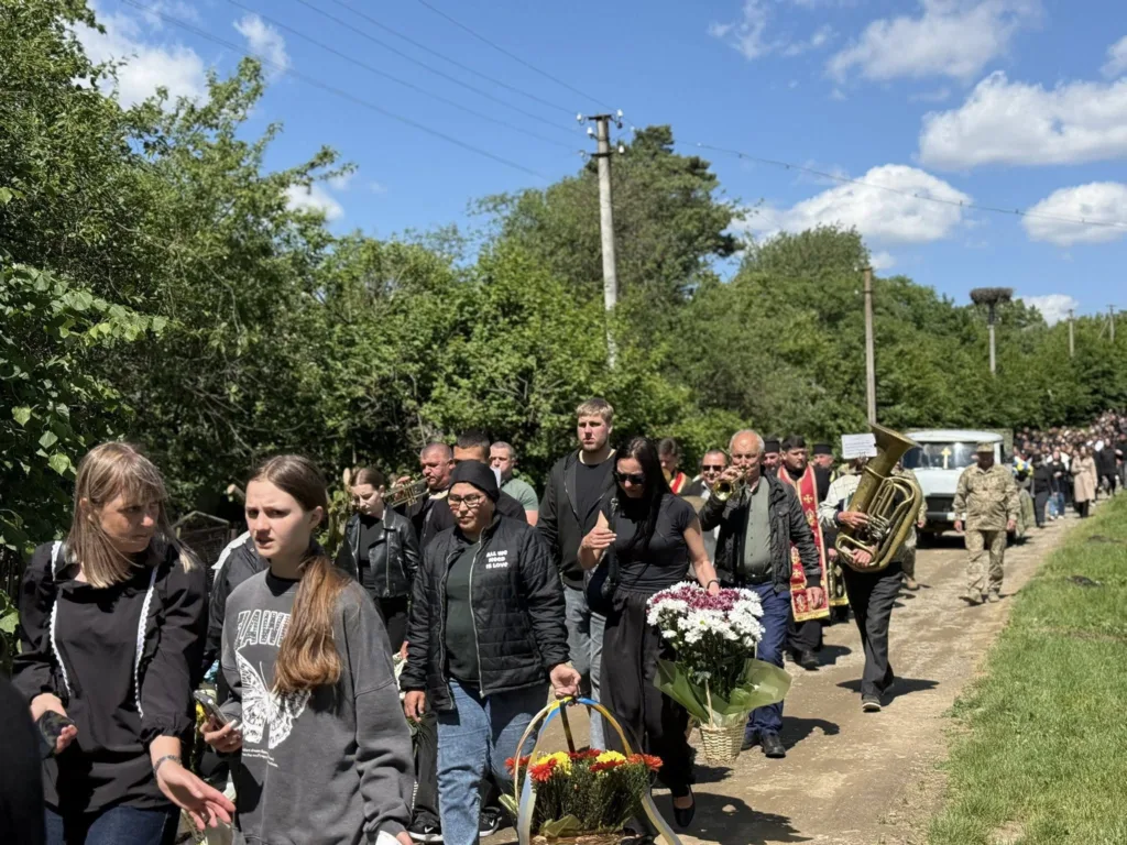 Люди йдуть селом на похорон із квітами