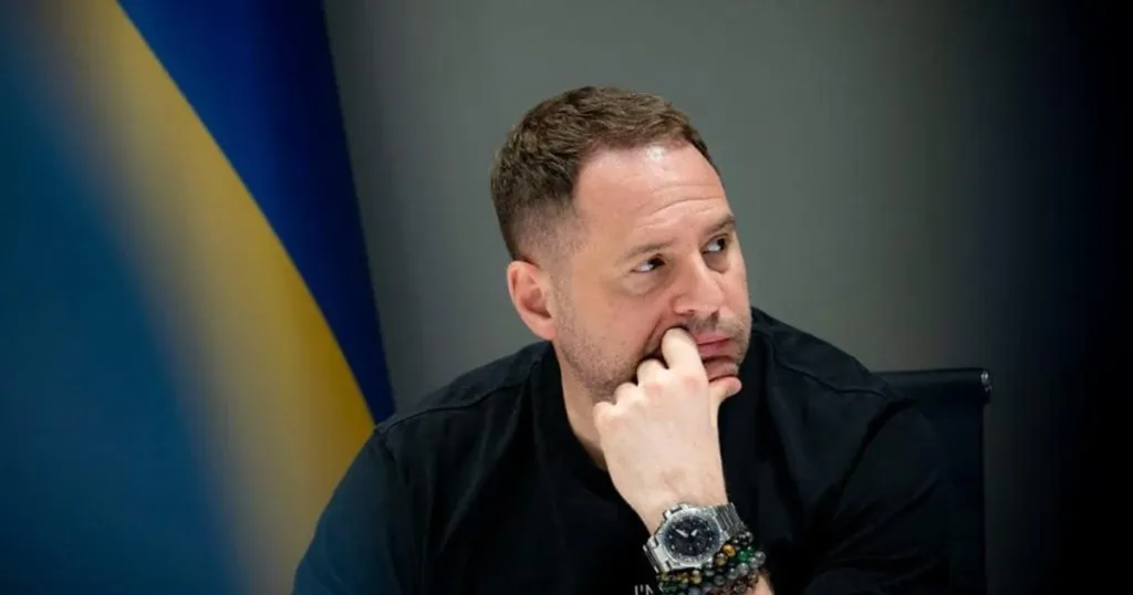 Чоловік задумливо сидить біля прапора України